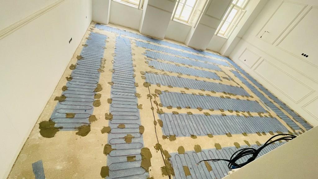 Verlegung elektrischer Fußbodenheizungsmatten auf Estrich in einem hellen Wohnraum